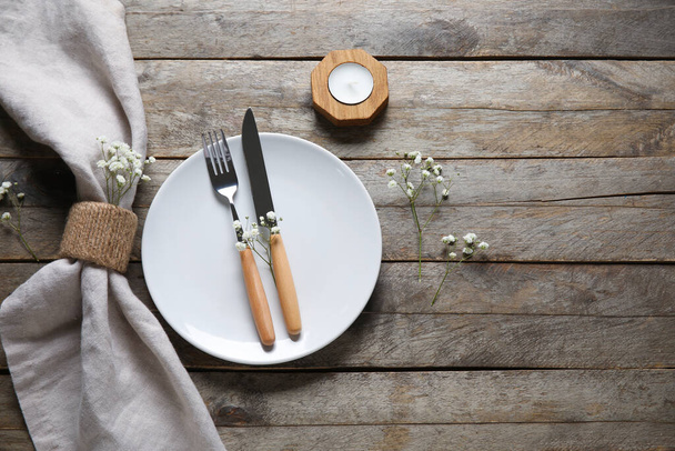 Plate with folded napkin, cutlery and candle on brown wooden background - Fotoğraf, Görsel