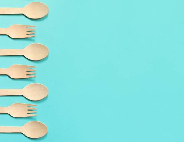 Wooden disposable forks and spoons on a blue background, top view. Eco friendly disposable kitchen utensils, copy space. Flat lay - Photo, Image