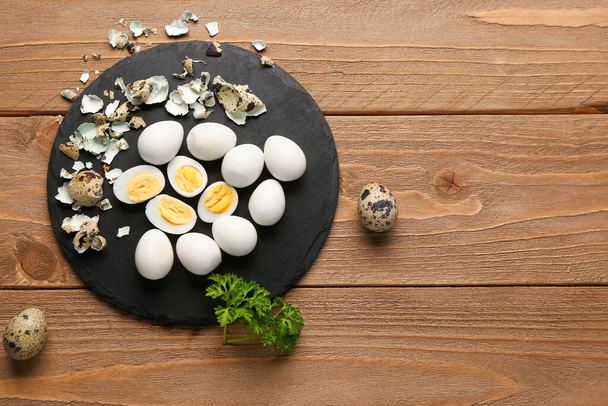 Board of boiled quail eggs with shells on wooden background - Фото, изображение