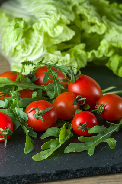 Joukko punainen kypsä tomaatti kivi leikkuulauta vihreät lehdet ja kiinalainen kaali taustalla - Valokuva, kuva