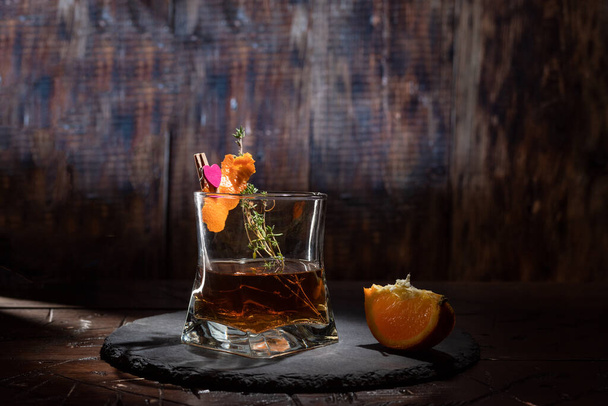 Glass of whiskey garnished with spices and orange. A glass of alcohol on the table. Composition with a glass. Front view. - Foto, afbeelding