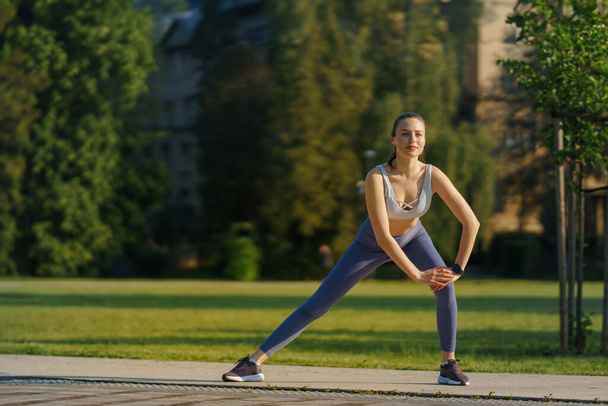 Full lenght portrait of beautiful fitness woman stretching before outdoor workout in the city park. Healthy lifestyle concept. Copy space. - Фото, зображення