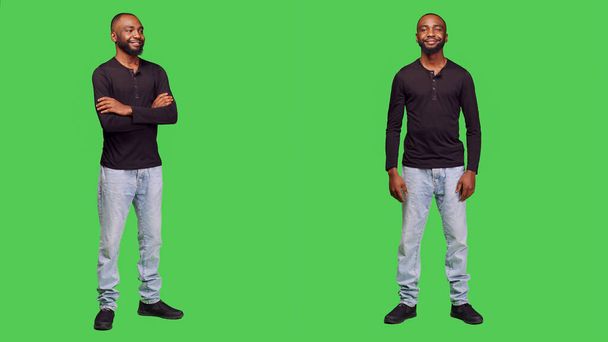 Optimistic adult standing over green screen backdrop, posing in studio and smiling on camera. Happy young model feeling positive wearing jeans and shirt, cheerful stylish person. - Photo, Image