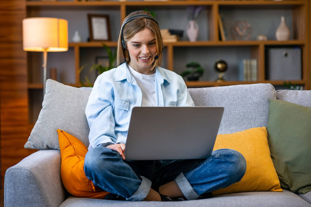 Videokonference. Usmívající se mladá žena s webovým hovorem na notebooku doma, mluvení před kamerou, zatímco sedí na pohovce v obývacím pokoji - Fotografie, Obrázek