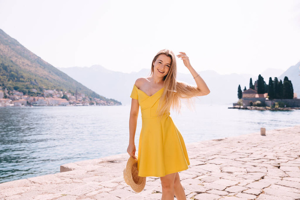 Jonge mooie vrouw draagt mooie gele jurk loopt door de kust - Foto, afbeelding