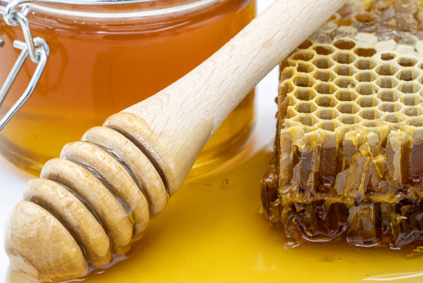 Closeup of jar of honey next to honeycomb and honey stick - Foto, Bild