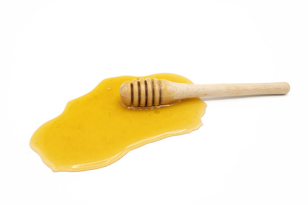 Honiglöffel auf verschüttetem Honig isoliert auf weißem Hintergrund - Foto, Bild