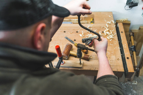 primo piano di un falegname maschio che crea un buco in una tavola di legno con un tutore, altri strumenti sullo sfondo. Foto di alta qualità - Foto, immagini