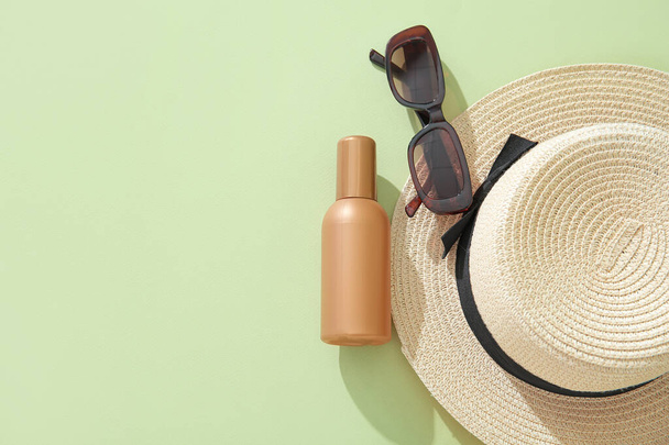 Бутылка крема от загара в солнцезащитных очках и летняя шляпа на зеленом фоне - Фото, изображение