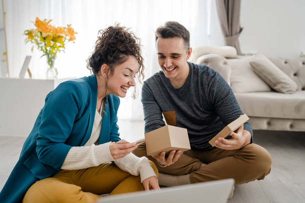 man hold and read greeting card while holding and opening presents gift box at home together with his girlfriend while sitting on the floor happy smile copy space real people caucasian adult - 写真・画像