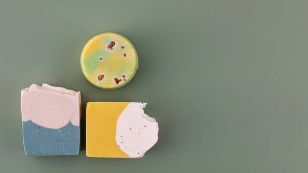 Pieces of different shapes and colors of handmade soap on a green background. The concept of natural cosmetics, hygiene. Copy space - Φωτογραφία, εικόνα
