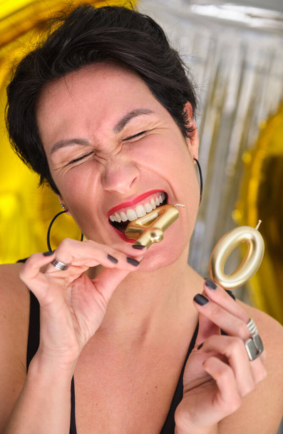 Kaukasische Frau lächelt in ihrer 40 Geburtstagsparty und beißt 40 goldene Geburtstagskerzen. - Foto, Bild