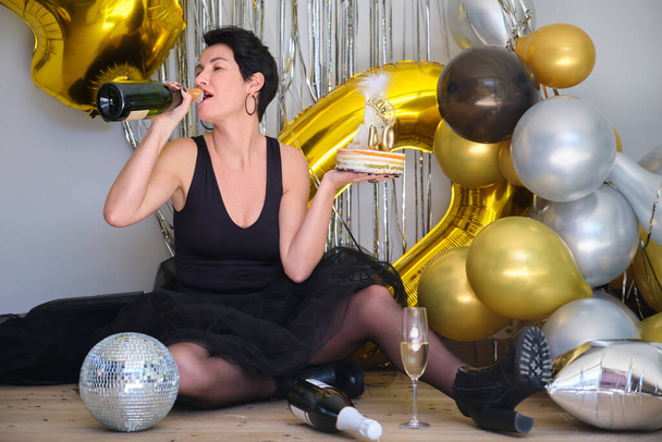 Biała kobieta pije szampana z butelki świętując swoje 40 urodziny na imprezie. - Zdjęcie, obraz