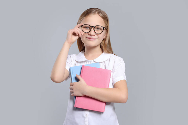 Portrait of cute girl in glasses with books on light grey background - Foto, imagen