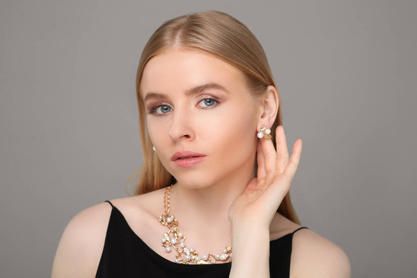 Beautiful young woman with elegant jewelry on gray background - 写真・画像