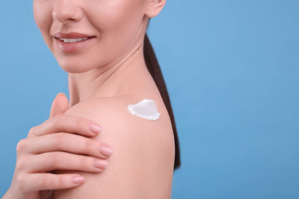 Woman with smear of body cream on her shoulder against light blue background, closeup. Space for text - Foto, imagen