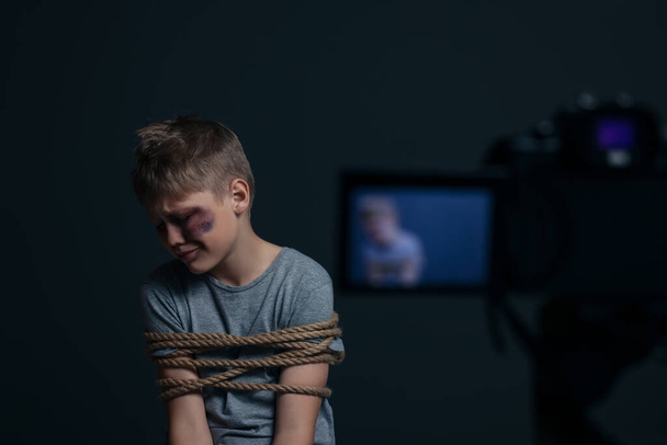 Little boy with bruises tied up and taken hostage near camera on dark background, selective focus - 写真・画像