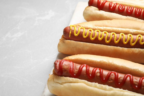 Fresh delicious hot dogs with sauces on light grey marble table, closeup. Space for text - Fotografie, Obrázek