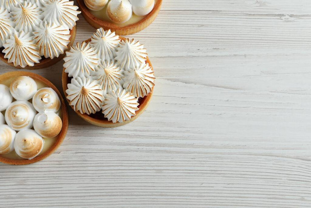 Many different tartlets with meringue on white wooden table, flat lay and space for text. Tasty dessert - Fotoğraf, Görsel