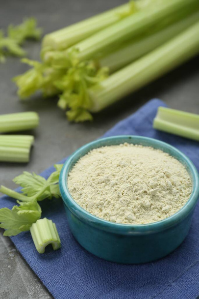 Natural celery powder in bowl and fresh stalks on grey table - Foto, afbeelding