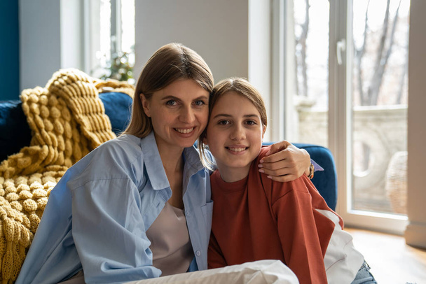 Mother-daughter friendship. Portrait of happy smiling mother and teen daughter hugging looking at camera, mom and teenage kid enjoying staying at home together on weekend - Foto, Imagen