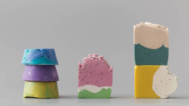 Pieces of different shapes and colors of handmade soap on a grey background. The concept of natural cosmetics, hygiene. - 写真・画像
