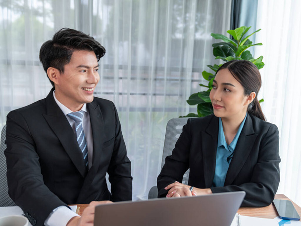 Two Asian office workers discussing and working together in corporate office workplace. Coworkers smiling and planning business work in friendly working environment in corporate workspace. Jubilant - Photo, Image