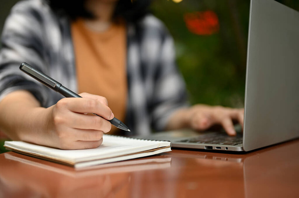 Immagine ritagliata di una giovane studentessa asiatica o di una freelance che lavora ai suoi compiti su un computer portatile in un caffè all'aperto. - Foto, immagini