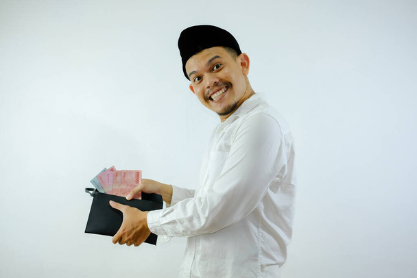 Seitenansicht eines muslimischen Asiaten, der glücklich lächelt, wenn er Geld aus seinem Portemonnaie nimmt - Foto, Bild