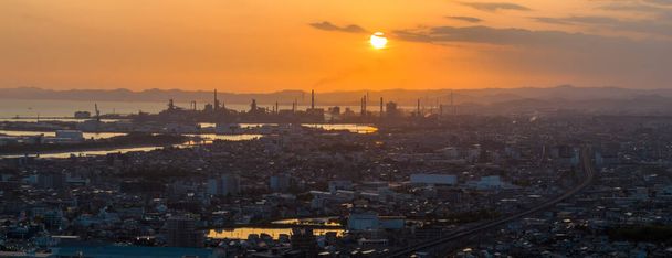 Gün batımında, endüstriyel bacalar ve şehir üzerinde, turuncu gökyüzünde alçak güneşin panoramik hava görüntüsü. Yüksek kalite fotoğraf - Fotoğraf, Görsel