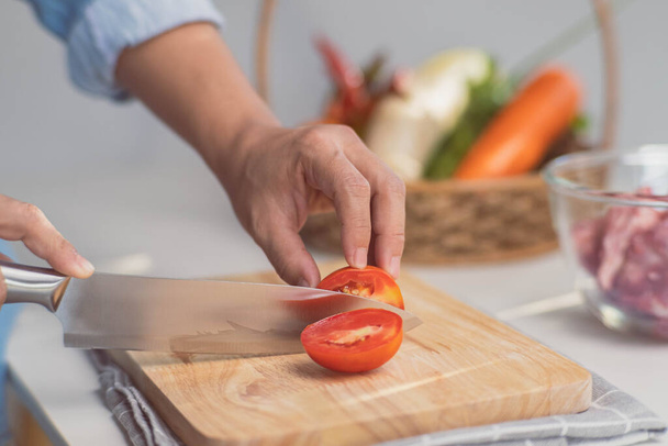 Cocinar - Las manos del chef están cortando tomates en la tabla de cortar en la cocina. Preparación de caldo de cerdo con verduras (caldo) en una olla. Receta casera de caldo. - Foto, imagen