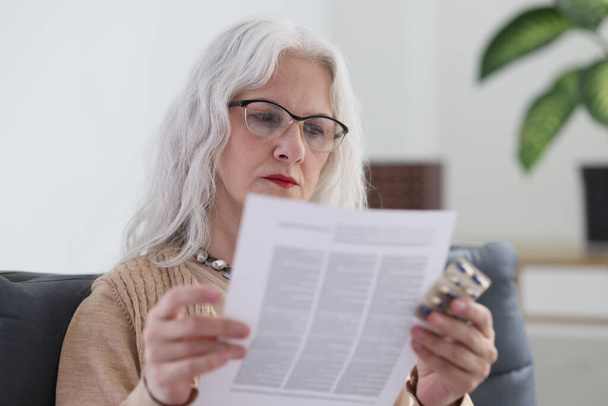 Vanhempi silmälasipäinen nainen lukee ohjeet lääketieteelle, jossa on muovinen läpipainopakkaus kapseleilla. Iäkkäät naiset käyttävät lääkkeitä ikään liittyvien sairauksien hoitoon - Valokuva, kuva