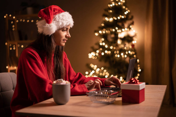 Compras en línea de Navidad. Compradora con portátil. Mujer compra regalos, prepararse para la víspera de Navidad, sentado en la mesa con caja de regalo. Vacaciones de invierno ventas. Copiar espacio - Foto, imagen