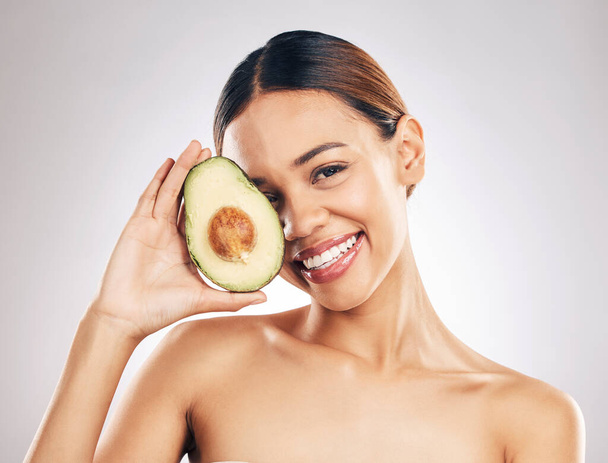 Woman, skincare and avocado in studio portrait for health, wellness or facial glow by white background. Girl, model and healthy skin with fruit, makeup or cosmetics for self care, aesthetic and smile. - Photo, image