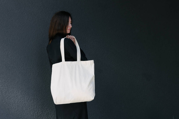 Woman holding white textile eco bag against urban city background. Ecology or environment protection concept. White eco bag for mock up. - Φωτογραφία, εικόνα