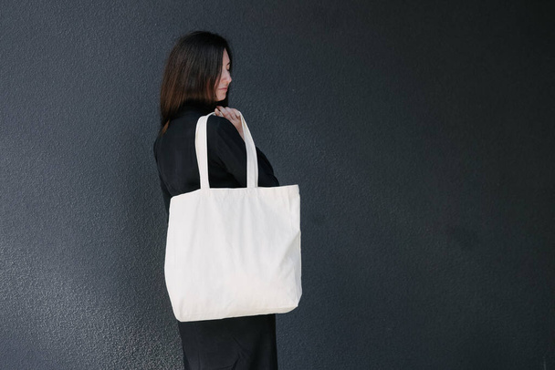 Woman holding white textile eco bag against urban city background. Ecology or environment protection concept. White eco bag for mock up. - Foto, imagen