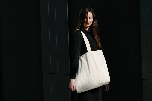 Woman holding white textile eco bag against urban city background. Ecology or environment protection concept. White eco bag for mock up. - Foto, immagini