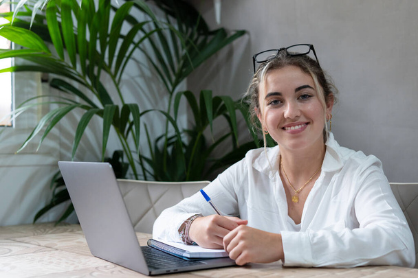 Portrait of smiling millennial caucasian female student sit at desk at home study online on laptop. Happy young cheerful woman use computer take distant course or training. Education concept. - Foto, imagen