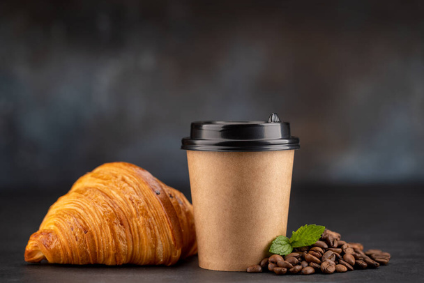 Aromatische koffie in een papieren beker gecombineerd met een schilferige croissant. met kopieerruimte - Foto, afbeelding