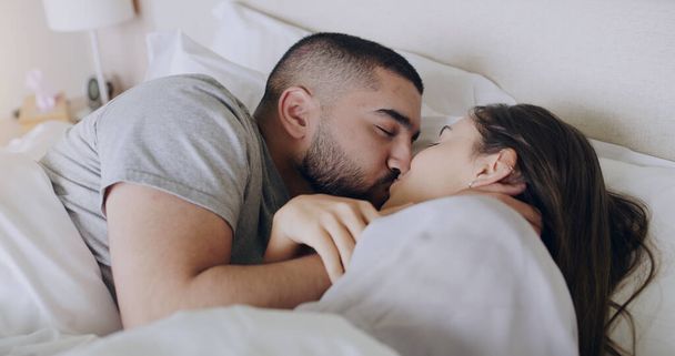Couple, kiss and bedroom for love, care and romance of intimacy, special moment and quality time together at home. Man, woman and kissing partner for relationship, honeymoon and relax in the morning. - Foto, imagen