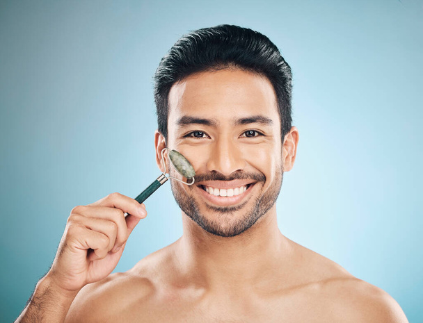 Happy man, portrait or face massage with jade roller, facial product for healthy skincare on studio background. Relaxing, grooming treatment or male model smiling with dermatology cosmetics or beauty. - Photo, Image