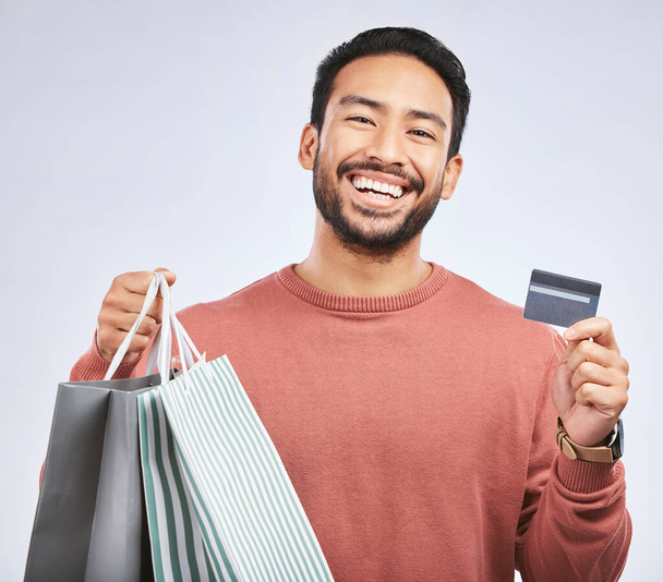 Man is laughing with shopping bag, credit card and happy about discount at boutique isolated on studio background. Humor, funny and male person with payment for purchase, luxury and retail with sale. - 写真・画像