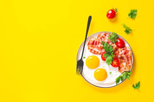 Huevos fritos y tocino con tomates cherry en plato, desayuno, keto, almuerzo a dieta paleo sobre fondo amarillo - Foto, imagen