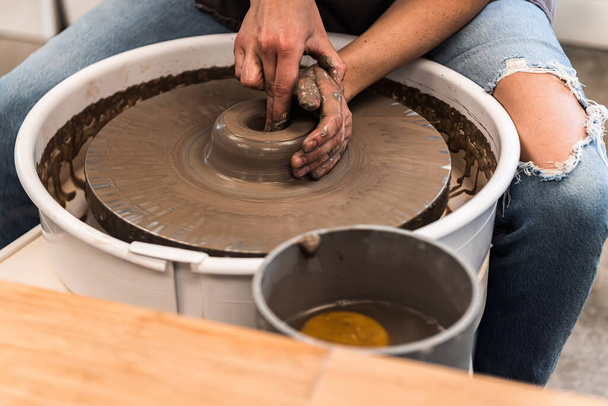 Woman working on a pottery wheel shaping the brown clay in a pottery studio - Foto, Imagem