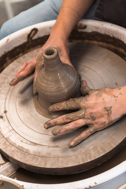 Woman working on a pottery wheel shaping the brown clay vase with wet hands - Φωτογραφία, εικόνα