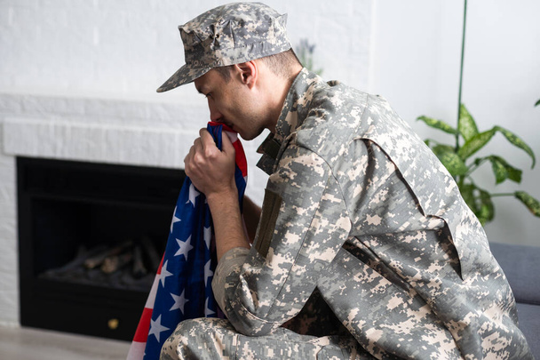 расстроен американский солдат, держащий флаг США во время плача в день памяти. - Фото, изображение