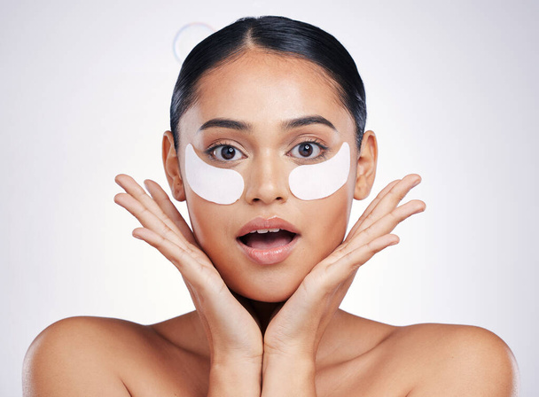 Face, eye mask and a woman in studio for beauty glow, dermatology or natural cosmetics. Portrait of surprised person with skincare patch for facial self care with wow results on a white background. - Fotografie, Obrázek