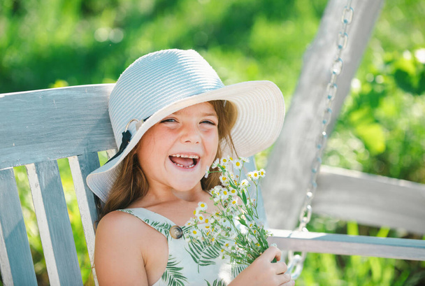 Portrait of a sweet little child enjoying flowers aroma, having fun in spring park. Little kid on meadow with wild flower. Happy child outdoors in spring field - Фото, изображение