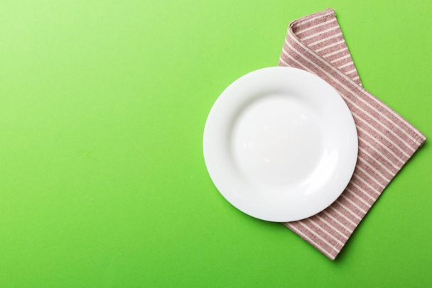 Top view on colored background empty round white plate on tablecloth for food. Empty dish on napkin with space for your design. - Fotó, kép