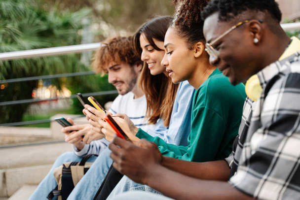 Молодая афроамериканка пользуется мобильным телефоном вместе с многорасовой группой друзей - Фото, изображение